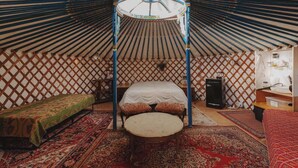 Een traditioneel ingerichte joert met een bed, een tafeltje en een hanglamp.