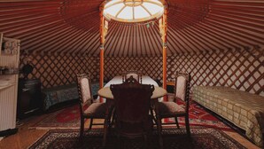 Ein traditionelles Jurten-Interieur mit einem runden Tisch in der Mitte, zwei Stühlen und einem Bett.