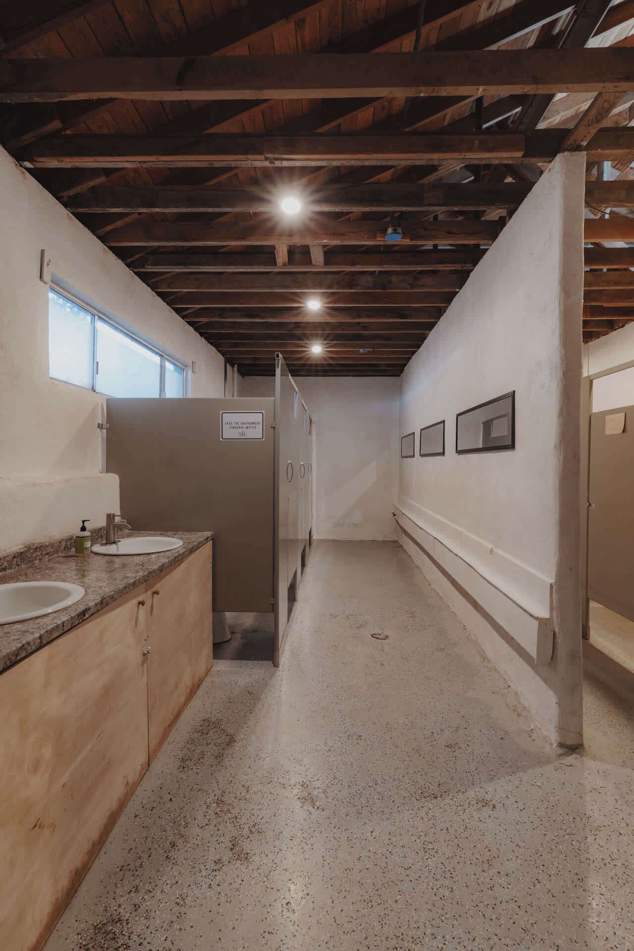 A narrow hallway with a sink and mirror on the left, wooden cabinets, and a sign indicating a water fountain.