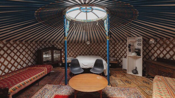 Et traditionelt yurt-interiør med seng, to stole, et lille bord og et dekorativt baldakin.