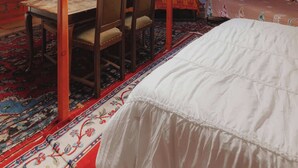 A traditional yurt interior with a central wooden canopy, a dining table with chairs, and a bed with a white bedspread. - Glamping yurt at a nature retreat Sequoia Highland (Dunlap)