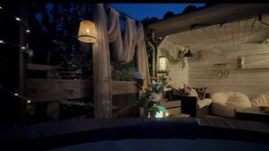 A cozy outdoor seating area with wooden furniture, string lights, and decorative plants.