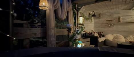A cozy outdoor seating area with wooden furniture, string lights, and decorative plants.