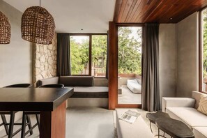A modern interior with a stone wall, a wooden ceiling, a dining area, a sofa, and a view through a glass door. - Siwa Jungle Sol B2-101 Beach Club Access (Tulum)