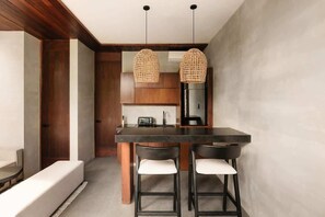 A modern kitchen with a dark countertop, two bar stools, and hanging wicker pendant lights. - Siwa Jungle Sol B2-101 Beach Club Access (Tulum)