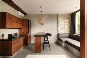 A modern kitchen with wooden cabinets, a central island, and a stone accent wall. - Siwa Jungle Sol B2-101 Beach Club Access (Tulum)