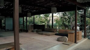 An outdoor seating area with a thatched roof, cushioned seating, and a wooden table. - Siwa Jungle Sol B2-101 Beach Club Access (Tulum)