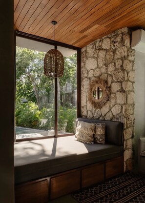 A room with a stone wall, a woven light fixture, a round mirror, and a bench with cushions. - Siwa Jungle Paradise Retreat C1-003 Beach Club (Tulum)
