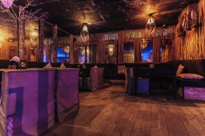 A rustic interior with wooden floors, tables, and chairs, and a bar area with stools. - Siwa Jungle Paradise Retreat C1-003 Beach Club (Tulum)