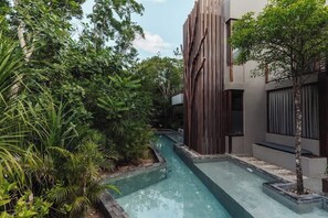 A modern building with vertical wooden slats, a narrow water channel, and lush greenery. - Siwa Jungle Paradise Retreat C1-003 Beach Club (Tulum)