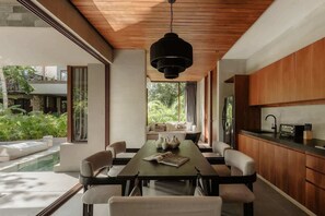 A modern dining area with a long table, chairs, and a hanging light fixture. - Siwa Jungle Paradise Retreat C1-003 Beach Club (Tulum)