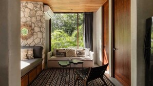 Un rincón acogedor con pared de piedra, un banco acolchado, un sofá con cojines decorativos, una mesita y una silla.