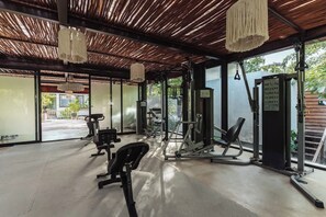 Ein Fitnessraum mit Trainingsgeräten, großen Fenstern und einer Holzbalkendecke.