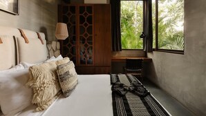 Un dormitorio con cama, almohadas, una alfombra tejida, un armario de madera y una ventana con vistas a follaje.