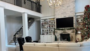 A spacious living room with a large white sectional sofa, a fireplace, and a Christmas tree. - SPACIOUS 4-bdrm sleeps 10+,heated porch & tv’s, pool,hot tub,play room (Oxford)