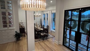 A spacious dining area with a chandelier, wooden flooring, and a view through a large window. - SPACIOUS 4-bdrm sleeps 10+,heated porch & tv’s, pool,hot tub,play room (Oxford)