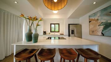 A modern kitchen with a central island, bar stools, a refrigerator, and a hanging light fixture.