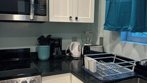 A kitchen with white cabinets, a stainless steel microwave, a stove, and a coffee maker. - ROSE COTTAGE-Tranquility steps from Grace Bay Beach and Grace Bay Strip! (Grace Bay)