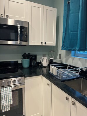 A kitchen with white cabinets, a stainless steel microwave, a stove, and a coffee maker. - ROSE COTTAGE-Tranquility steps from Grace Bay Beach and Grace Bay Strip! (Grace Bay)
