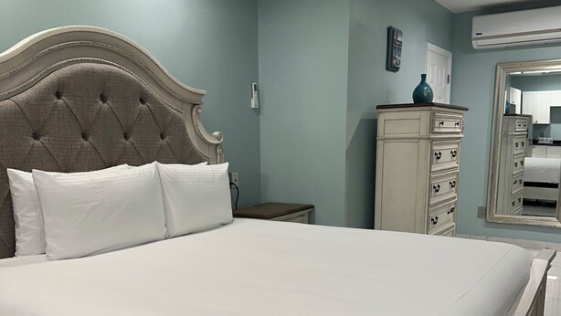 A neatly made bed with a tufted headboard, a bedside table, a dresser, and a ceiling fan in a room with light blue walls and a tiled floor. - ROSE COTTAGE-Tranquility steps from Grace Bay Beach and Grace Bay Strip! (Grace Bay)