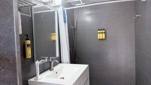 A modern bathroom with a white sink, a mirror, and a shower area. There are toiletries on the wall and a towel rack. - ROSE COTTAGE-Tranquility steps from Grace Bay Beach and Grace Bay Strip! (Grace Bay)