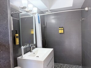 A modern bathroom with a white sink, a mirror, and a shower area. There are toiletries on the wall and a towel rack. - ROSE COTTAGE-Tranquility steps from Grace Bay Beach and Grace Bay Strip! (Grace Bay)
