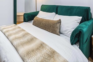 A bed with a green upholstered headboard, white pillows, and a patterned throw blanket.