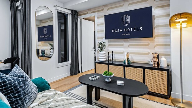 Ein modernes Hotelzimmer mit einer Couch, einem runden Tisch, einem Konsolentisch mit Dekoration und einem an der Wand befestigten Schild.