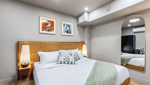 Ein modernes Hotelzimmer mit einem großen Bett, zwei Nachttischen mit Lampen, einem großen Spiegel und zwei gerahmten Kunstwerken an der Wand.