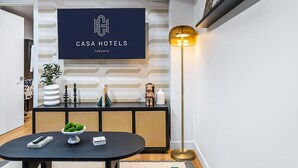 Eine moderne Hotelhalle mit einem schwarzen runden Tisch, einer Zimmerpflanze, einem Konsolentisch mit Dekoration und einer Stehlampe. Auf einem Schild steht: CASA HOTELS TORONTO.