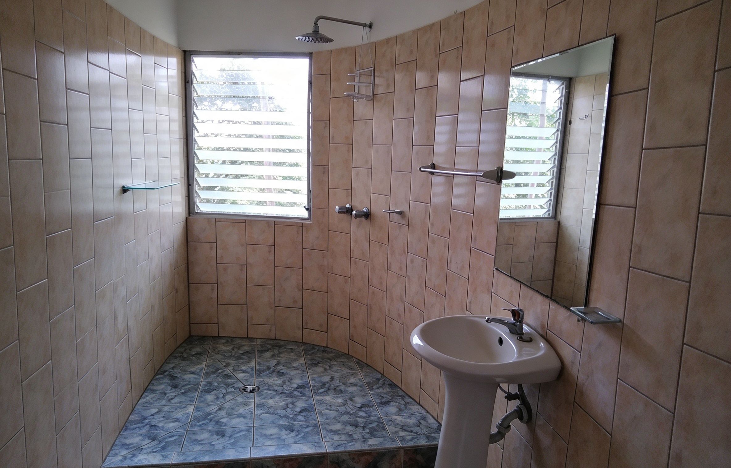 A bathroom with a shower, a sink, and a window.