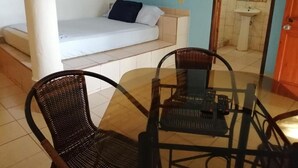 Una habitación con cama, una mesa de vidrio con sillas, un pequeño sofá y un baño con lavamanos.