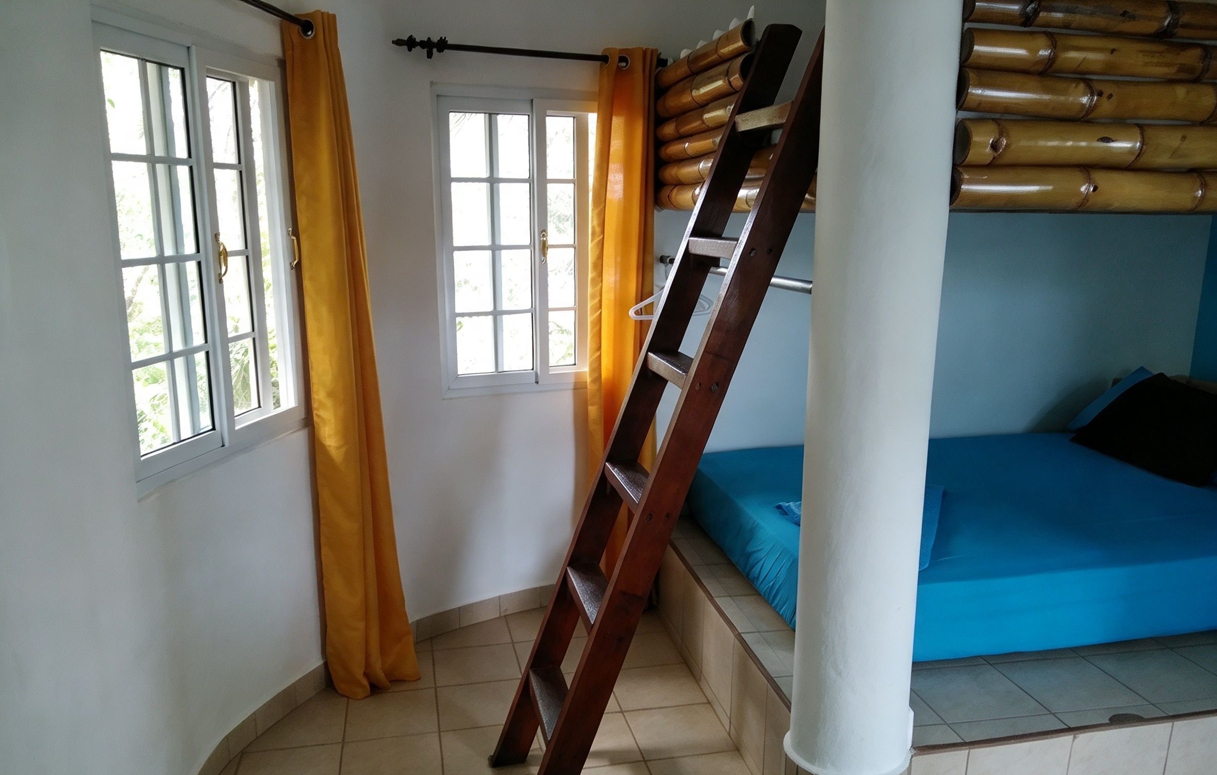 Habitación con literas, una escalera, dos ventanas con cortinas y vista al exterior.