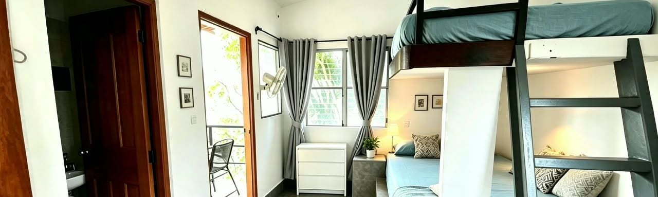 Una habitación con literas, un escritorio, una silla y un ventanal con cortinas.