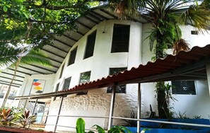 Un bâtiment à l’extérieur blanc, doté de nombreuses fenêtres et d’un espace d’entrée abrité surmonté d’un toit en métal.