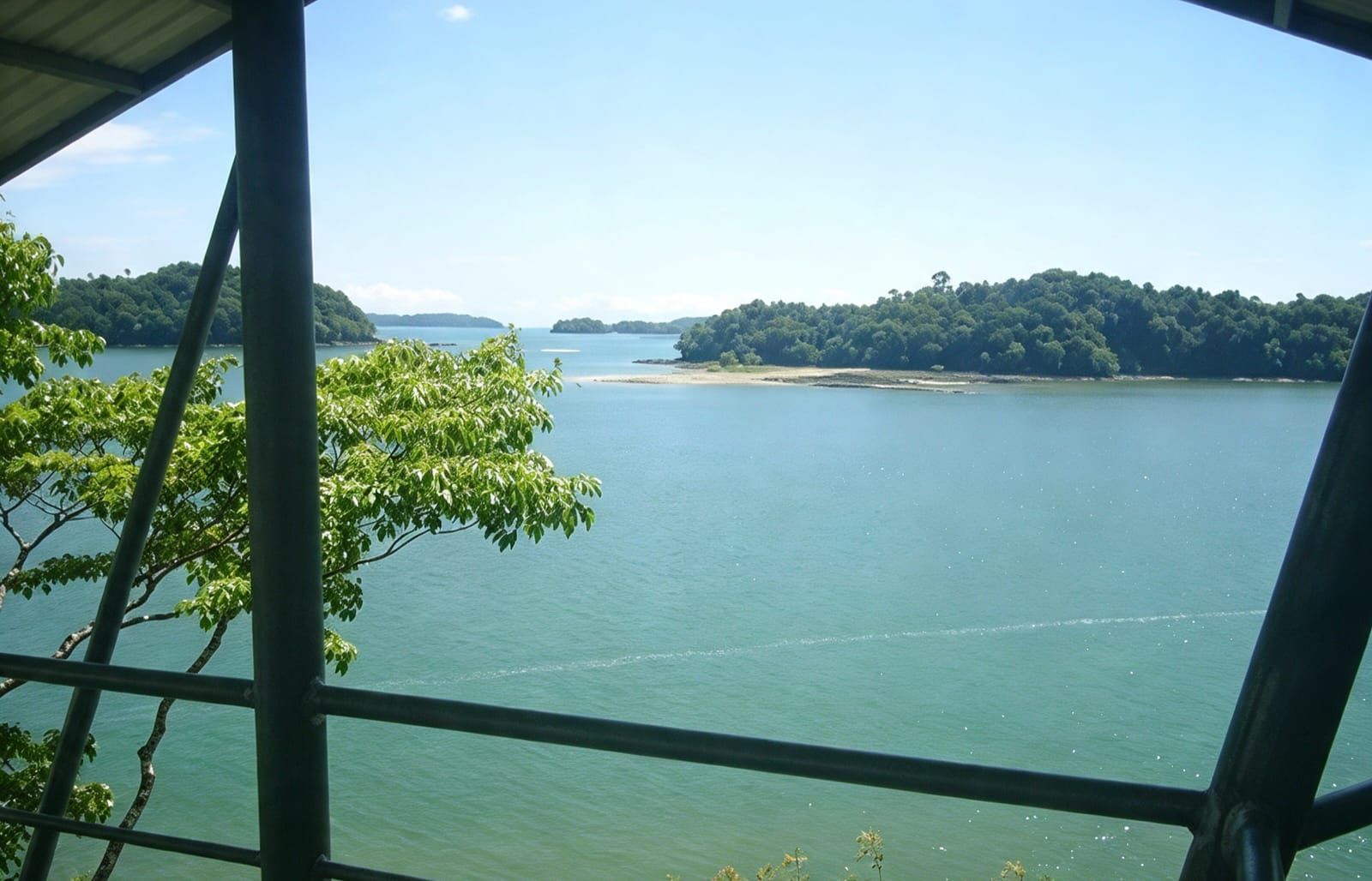 A view of a calm lake with a forested island in the distance, viewed from a covered area with metal railings.