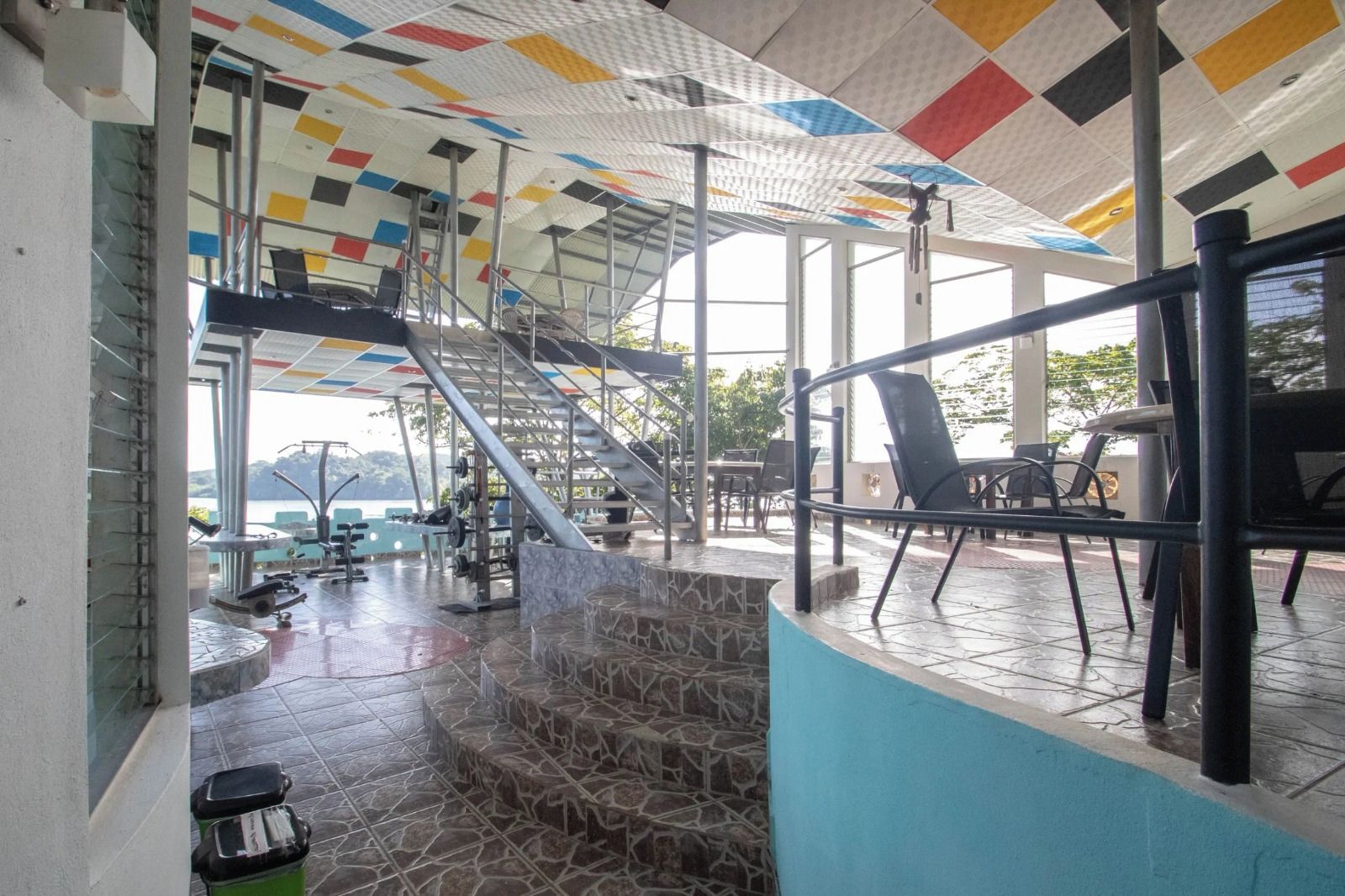 Ein überdachter Außenbereich mit Treppe zu einer Terrasse, ausgestattet mit Fitnessgeräten und Sitzmöbeln.