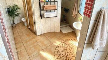 Un baño con suelo de baldosas, zona de ducha, inodoro y lavabo.