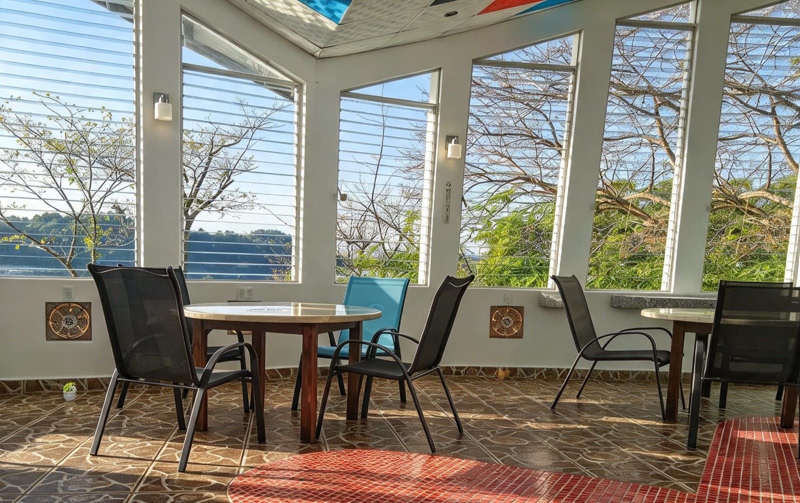 Un patio iluminado por el sol con vista al mar, con una mesa redonda y sillas, y piso de baldosas.