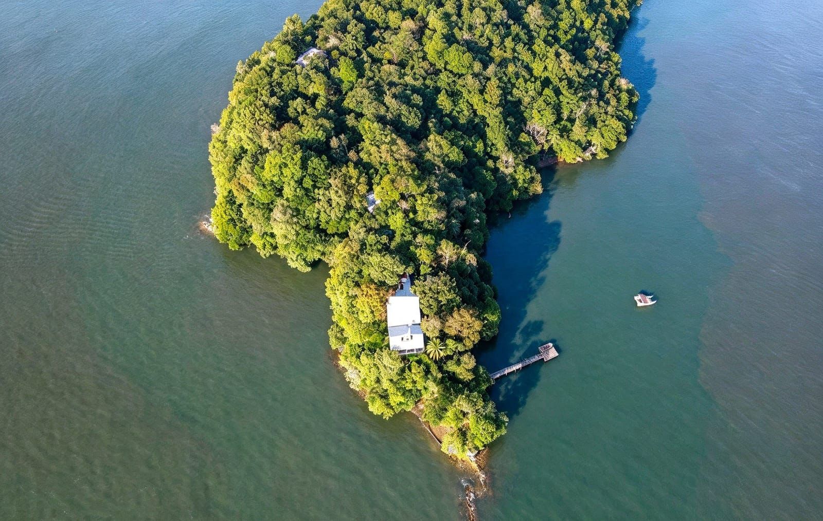 Eine Luftaufnahme einer kleinen Insel mit dichtem Grün, einem Steg und einem Gebäude.