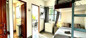 Ein Schlafzimmer mit Etagenbetten, einem Nachttisch, einem Sessel, einem Fenster mit Vorhängen und Blick auf Grünfläche.