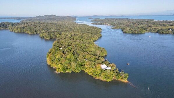 An aerial view of a lush, green island with a small building, surrounded by calm waters and other islands in the distance.