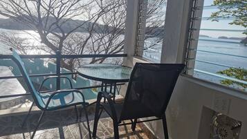 Un balcón con una mesa y sillas de vidrio, con vistas al agua y árboles.