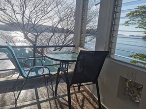 Un balcon avec une table et des chaises en verre, donnant sur une étendue d’eau et des arbres.