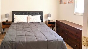 A neatly made bed with a grey quilt, two bedside tables with lamps, and a wooden dresser.