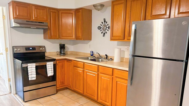 A kitchen with wooden cabinets, a stainless steel refrigerator, an oven, and a coffee maker.