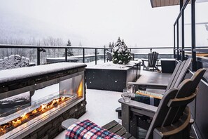 Une terrasse enneigée avec une cheminée en pierre, des sièges d’extérieur et une vue sur un paysage hivernal.