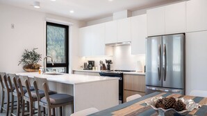 Une cuisine moderne avec des meubles blancs, un réfrigérateur en acier inoxydable et une table à manger en bois, accompagnée de chaises.