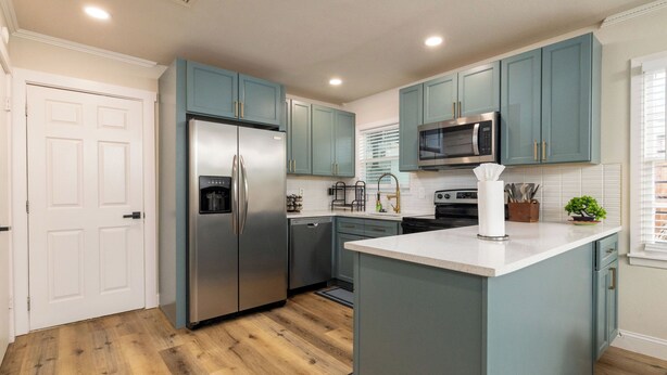 Une cuisine moderne avec des armoires de couleur turquoise, des appareils électroménagers en acier inoxydable et un îlot central.