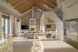 A spacious living area with a stone wall, a fireplace, a sofa, and a TV. - Sea View Petralis Residence   2 Bedroom apartment (Agios Nikolaos)